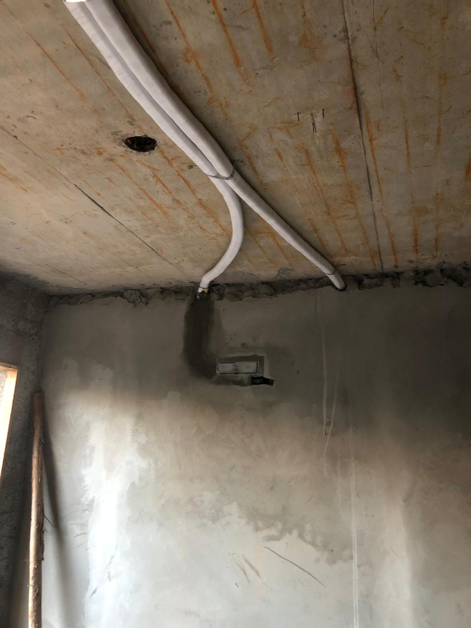 obra em fase de acabamento com tubulações brancas no teto de concreto e parede com reboco recebendo ponto elét