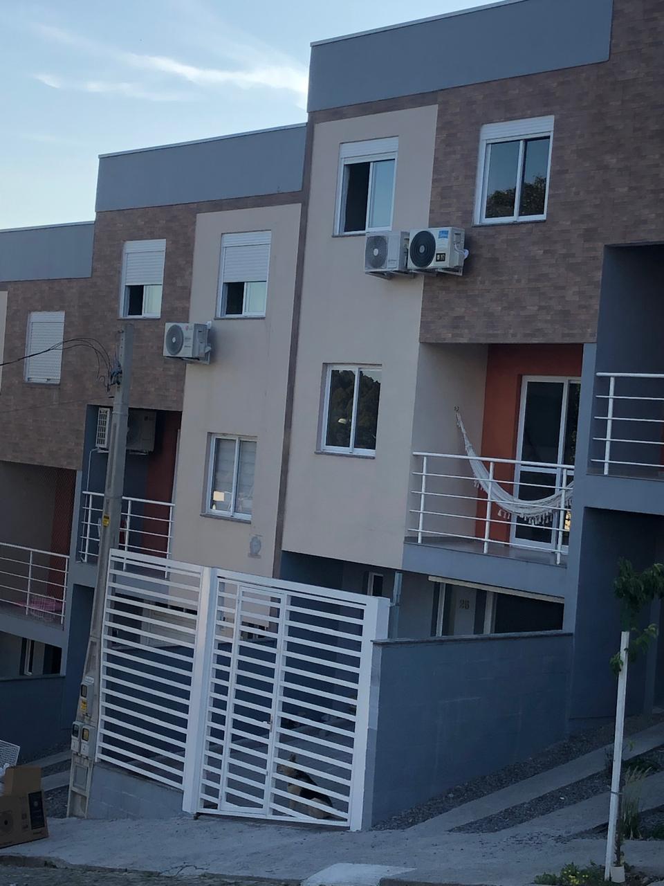 Fachada de prédio residencial de dois andares com revestimento em tijolinho marrom e pintura bege, muro e port